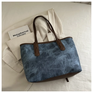 Close-up of blue denim tote bag with brown leather handles on a white fabric background