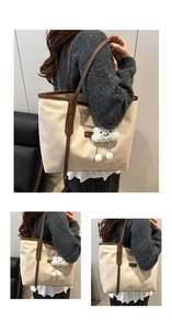 Detail of a beige canvas tote bag featuring brown leather straps and a plush cloud charm