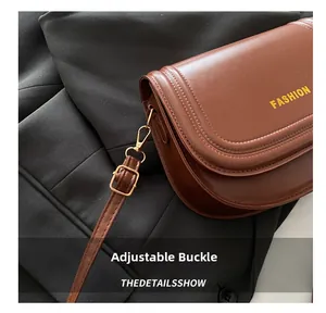 Macro detail of brown saddle bag with golden FASHION logo and adjustable buckle