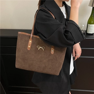 Brown suede tote bag with golden bow detail worn by a model in a stylish setting