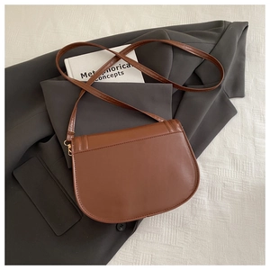 Detailed close-up of a vintage brown leather saddle bag on a gray suit jacket