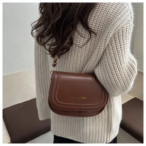 Detail of a brown leather saddle bag with gold FASHION lettering and adjustable strap