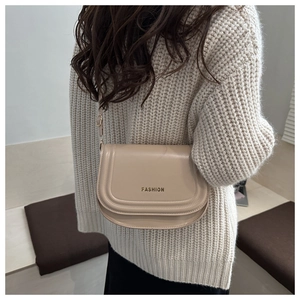 Detail of a beige matte leather saddle bag with Fashion text on a knit sweater