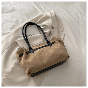 Detail of vintage brown suede tote bag with black leather straps on a white fabric surface