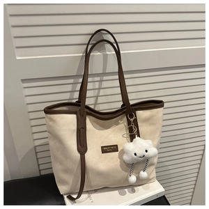 Detail of beige tote bag with brown leather trim and a white cloud plush keychain