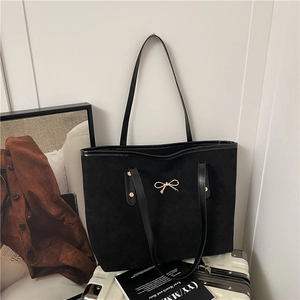 Sac fourre-tout chic en daim noir avec boucle dorée pour femmes sur une valise blanche