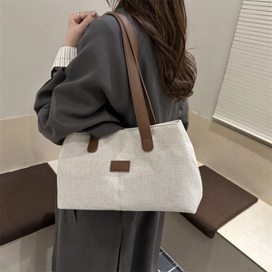Large beige canvas tote bag with brown leather handles worn by a model in a modern interior