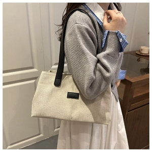 Large beige canvas tote bag with black handles shown on shoulder in a lifestyle setting