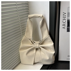 Detailed view of cream textured faux leather handbag featuring a large stylish bow