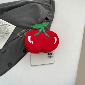Detailed view of red cherry-shaped shoulder bag with golden chain and phone for size