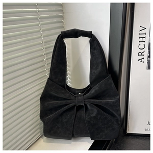 Detail of a black shoulder bag with a large bow design and matte suede texture