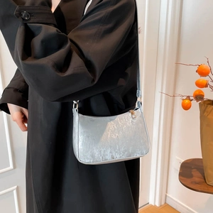 Minimalist silver underarm bag with metallic texture shown on black trench coat