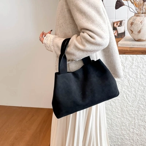 Minimalist black tote bag in matte suede leather shown on shoulder in stylish interior
