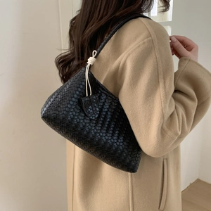 Sac à bandoulière tressé en cuir noir avec nœuds blancs porté avec un manteau en laine