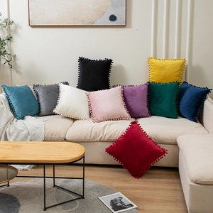 Solid velvet pillow cover with decorative pom-poms on a sofa in a cozy home setting