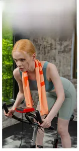 Orange cooling sports towel used by a model on a stationary bike in a gym setting