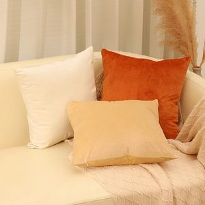 Modern velvet cushion covers in warm cream and orange tones on a leather sofa