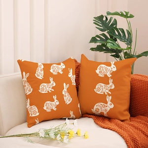 Bright orange Easter pillow covers with white rabbit print on a cozy sofa