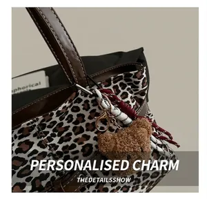 Detail of leopard print suede tote bag with brown leather handle and plush bear charm