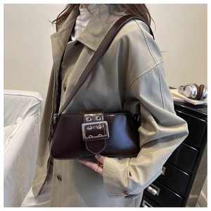 Sac bandoulière marron foncé avec boucle argentée porté sur un trench-coat beige élégant
