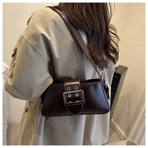Détail d'un sac sous le bras en cuir marron foncé avec boucle argentée porté par un modèle
