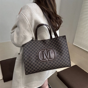 Chic 2025 brown tote bag with M-pattern print and dual handles worn by a model