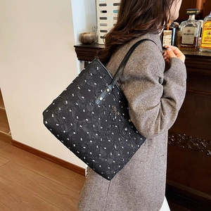 Grand sac cabas noir avec imprimés blancs et nœud doré porté à l'épaule pour femme