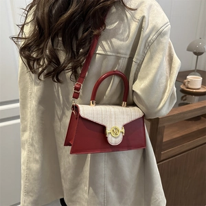 Elegant red leather and tweed crossbody bag with golden M buckle worn over a beige coat