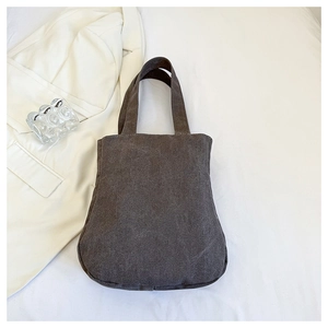 Flat lay of charcoal gray canvas tote bag on white blazer and fabric background
