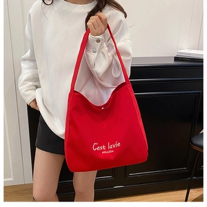 Detail of red canvas tote bag with C'est la vie print shown on a female shoulder
