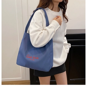 Close-up of blue tote bag featuring red C'est la vie embroidery on canvas fabric