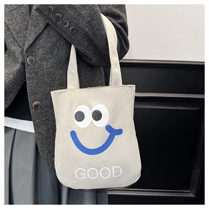 Detail of a beige canvas tote bag with a blue smiley face pattern and GOOD text