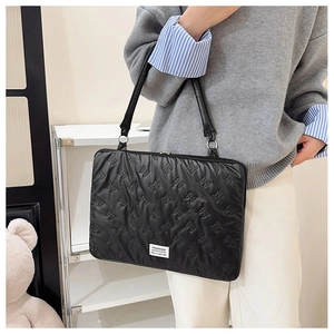 Quilted black laptop bag with bow pattern and metal ring handles shown on shoulder