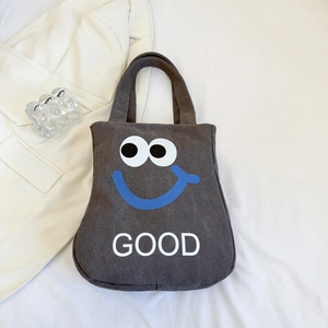 Detailed shot of dark gray canvas tote bag featuring unique cartoon face and GOOD text