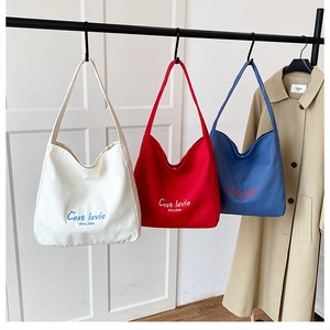 Detailed display of colorful canvas tote bags with C'est la vie slogan on black rack