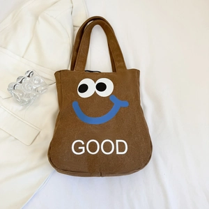 Detail of a brown canvas tote bag featuring an embroidered blue smile and GOOD text print