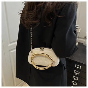 Detail of elegant beige crossbody bag with large gold wave ring and metal chain
