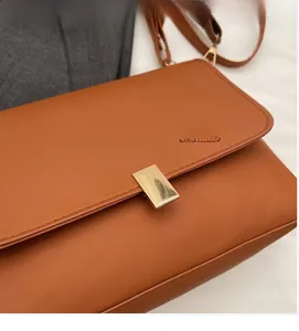 Detail of a brown leather crossbody bag featuring a classic gold rectangular metal clasp