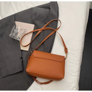 Close-up of brown faux leather shoulder bag with adjustable strap and golden metal buckle