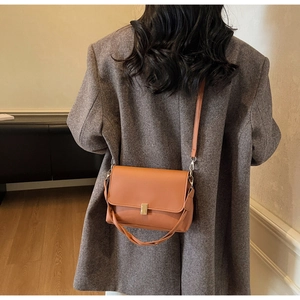 Brown vintage shoulder bag with golden buckle and woven handle on a stylish coat