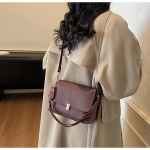 Detail view of the brown leather shoulder bag on a model wearing a beige trench coat