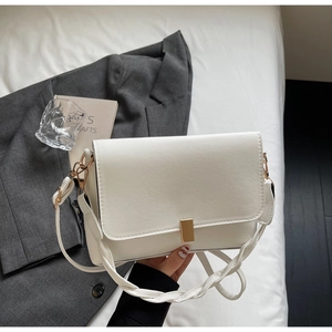 Close-up of a white shoulder bag with a gold rectangular buckle and braided strap detail