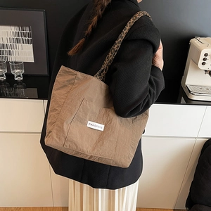 Brown nylon tote bag with leopard print shoulder straps in a minimalist indoor setting