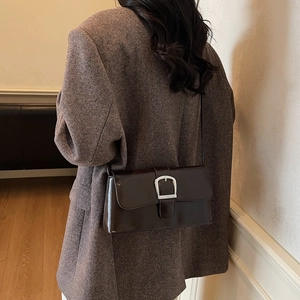 Brown leather baguette shoulder bag with silver buckle worn by a model in soft light