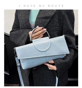 Detail of light blue handbag with crocodile texture, metal handle and stylish flap