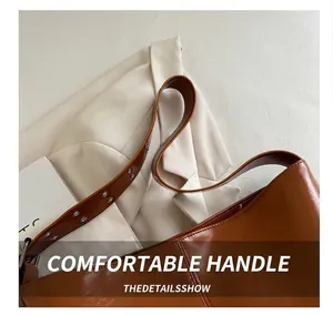 Detail of wide adjustable shoulder strap on brown patent leather bag with metal rivets