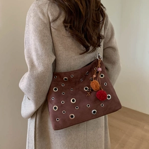 Brown suede bucket bag with metal eyelets and decorative charms on beige coat