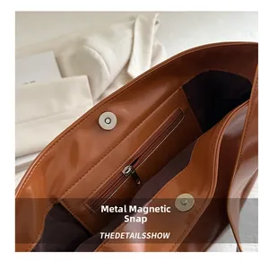 Detail of the magnetic buckle closure and internal zipper pocket on brown leather tote bag