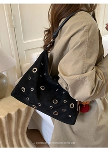 Detail of black suede tote bag featuring silver metal eyelets and a plush charm