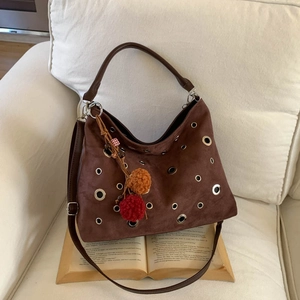 Detail of brown suede hobo bag with metal eyelets and decorative pom-pom on white sofa